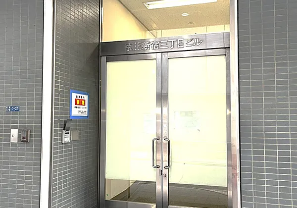 上に京王新宿三丁目と書いたこの銀枠の扉を引いて開き、ビルに入ってください